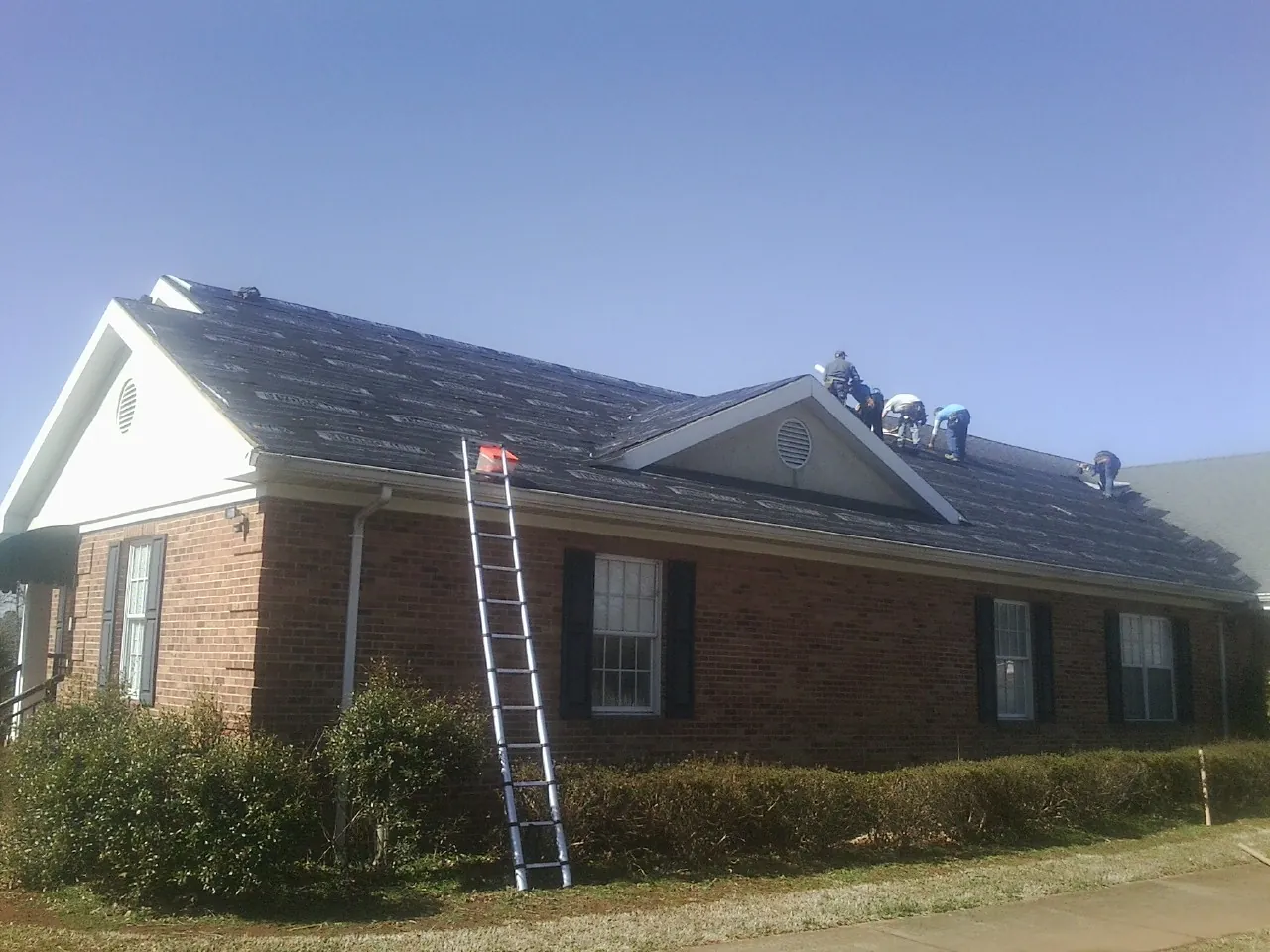 Crew tearing shingles off a brick ranch roof with a ladder set — Emergency Roof Repair work by our crew in Oradell
