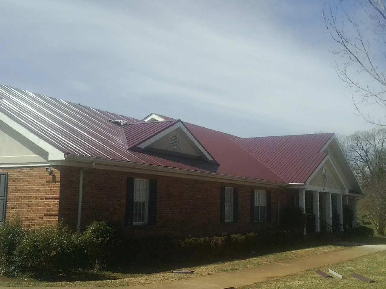 Red metal roof with gabled entries on a long brick building, from a Hail Damage Roof Repair job in Oradell