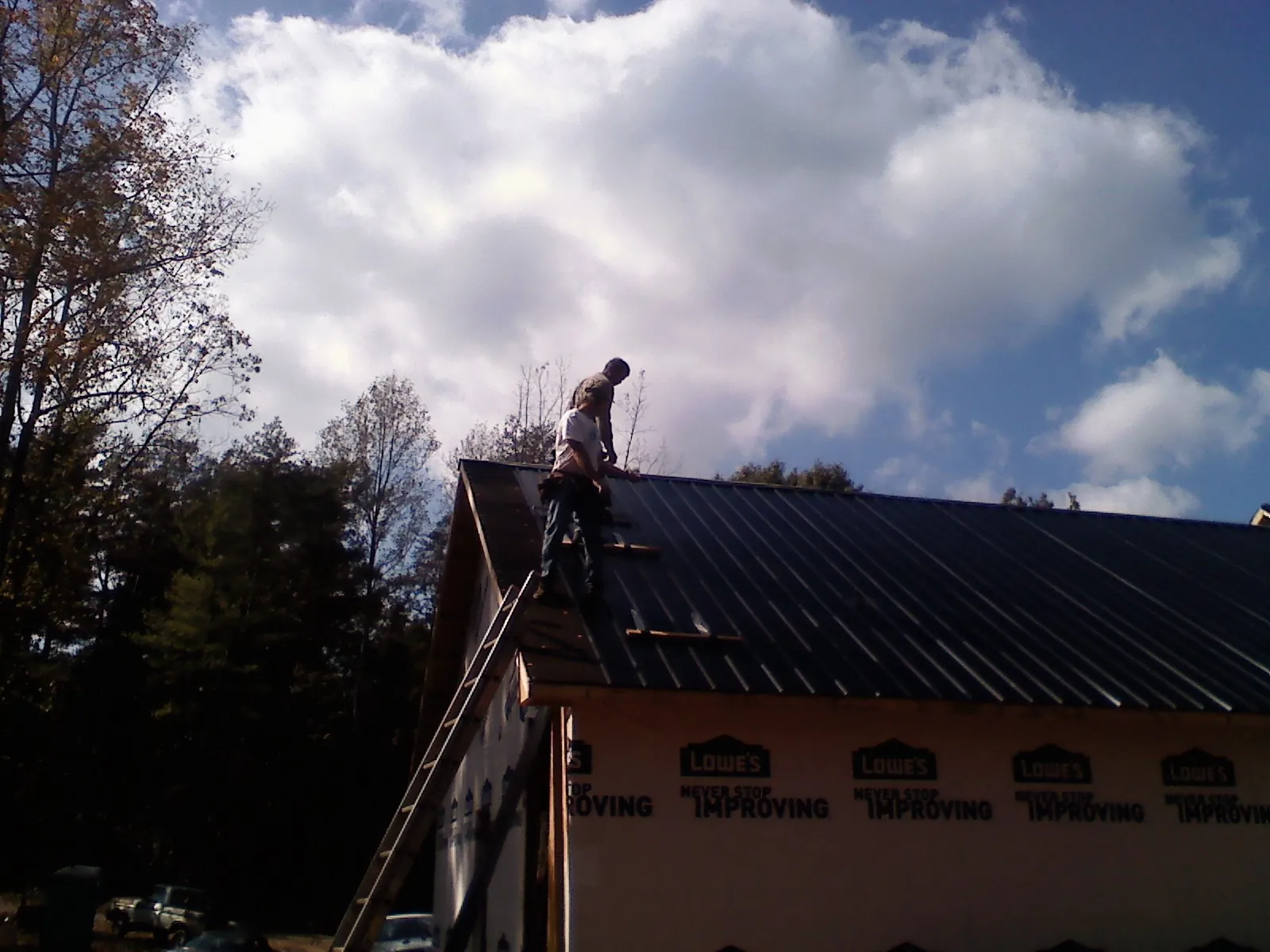 Roofer fastening dark metal panels high against a cloudy sky, from a Roof Inspection job in Oradell