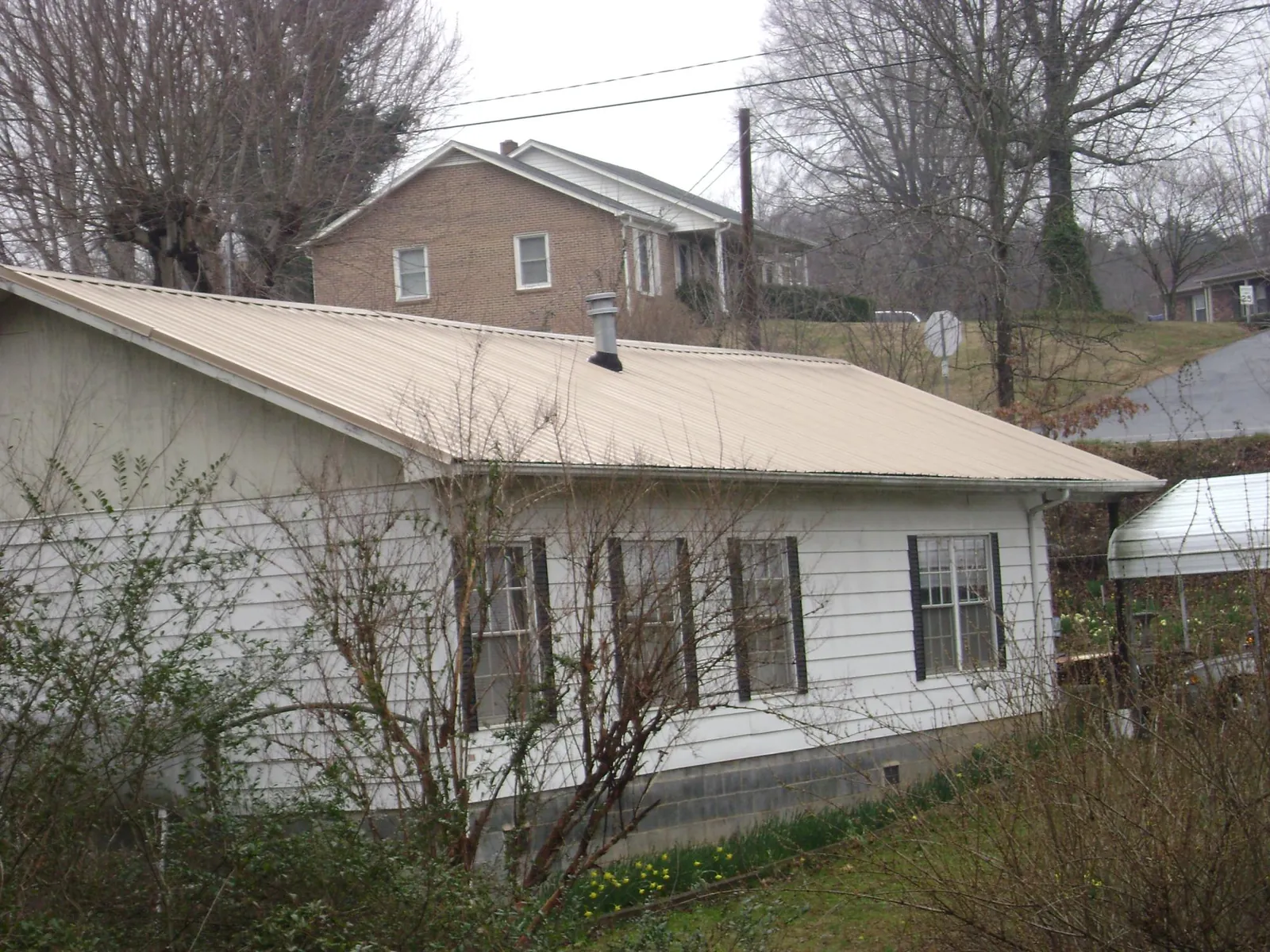 Tan metal roof on a white sided house set into a hillside — Commercial Roofing by Roofing Brothers in Oradell
